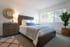 Bedroom with grey carpet large wood framed bed and large window and base board heater