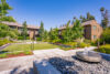 Stone water fountain in front of grassy tree lined area and 2 story apartment buildings.