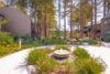 Stone water fountain in front of tree lined area and 2 story apartment buildings.